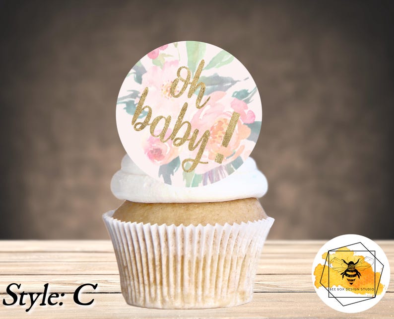 K&ouml;nnte beinhalten: Ein Cupcake, der mit einem runden, rosa und goldenen, floralen Cupcake-Topper verziert ist, auf dem "oh baby!" steht.