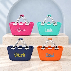 May include: Four rectangular canvas baskets with silver metal handles. The top left is hot pink with the name Alana, top right is teal with Lanis, bottom left is navy blue with Saira, and bottom right is orange with the name Esmé embroidered on them.