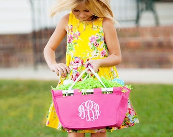 May include: A young girl in a yellow floral dress holds a pink canvas tote bag with white handles. The bag has a white monogram on the front. The bag is filled with green grass and Easter eggs.