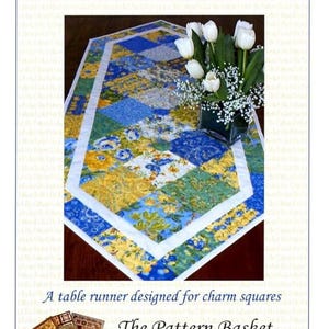 Puede incluir: Un camino de mesa Country Charm con un diseño de patchwork en tonos azules, amarillos y verdes. El camino de mesa tiene un borde blanco y presenta patrones florales. La imagen incluye el texto "Country Charm Table Runner" y "The Pattern Basket".