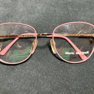 May include: Pink and gold-toned eyeglasses with a rounded frame design. The glasses have a delicate, feminine aesthetic, with the brand name "Mario Martinelli" visible on the arm and lens. The frame is a soft pink color.