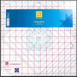 Può includere: Un righello per quilting bianco con un'etichetta blu e bianca che dice "EZ Quilting Pineapple". Il righello ha un motivo a griglia con linee blu e rosa. Il centro del righello ha un quadrato con le parole "Center Square" scritte all'interno.