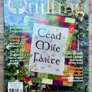 Op de afbeelding: De cover van het tijdschrift "Irish Quilting" toont een kleurrijk quiltontwerp met de woorden "Céad Míle Fáilte". Extra tekst bevat artikelen over quilttechnieken, St. Patrick's Day-projecten en lezersuitdagingen. Het tijdschrift is omgeven door groen gebladerte.