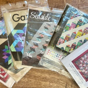 May include: A collection of eight quilting patterns featuring various designs, including "Rock Candy", "Gaze", "Seaside", "Diamond Log Cabin", and "Ferris Wheel".