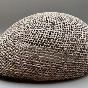 May include: A woven, light brown newsboy cap. The hat is made of a tightly woven material, creating a textured surface. The cap has a rounded crown and a small, curved brim. The overall design is simple and classic.