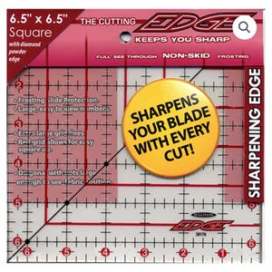Peut inclure: Une règle carrée en plastique transparent de 16,5 cm sur 16,5 cm avec des lignes de quadrillage rouges et une ligne diagonale noire. La règle a un bouton jaune avec le texte "Sharpens your blade with every cut!" imprimé dessus. La règle est étiquetée "The Cutting Edge" et "Keeps You Sharp".