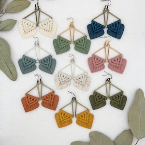 May include: Assortment of handmade macrame earrings with geometric triangle shapes and fringe details. The earrings are available in a variety of colors, including cream, teal, green, pink, white, orange, and yellow.