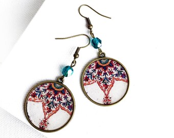Può includere: Un paio di orecchini pendenti con un design rotondo, bianco e rosso. Gli orecchini hanno un bead di cristallo blu turchese su ogni lato.