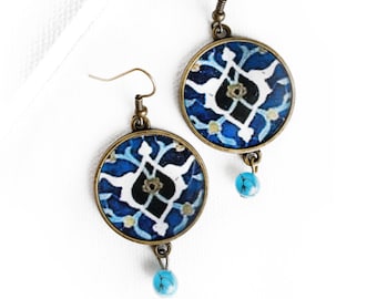 Può includere: Un paio di orecchini rotondi con motivo blu e bianco con perline turchesi. Gli orecchini hanno una finitura in bronzo.
