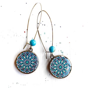 May include: A pair of dangle earrings with turquoise blue beads and round, patterned charms. The charms feature a blue, green, and white geometric design.