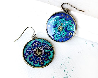Può includere: Un paio di orecchini rotondi con motivo floreale blu e verde con ganci in metallo dorato.