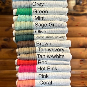 May include: A stack of quilted fabric items in various colors, including royal blue, pale blue, grey, green, mint, sage green, olive, forest green, brown, tan, red, pink, coral, orange, and purple. Each item has a contrasting border.