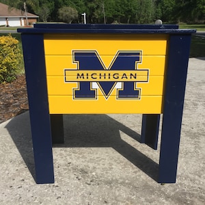 May include: A blue and yellow cooler with the University of Michigan logo and the word "MICHIGAN" printed on the front.