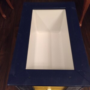 May include: A blue and yellow wooden cooler with a white interior. The cooler has a small drawer with a white knob.