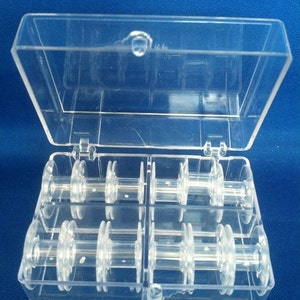 May include: A clear plastic box with a hinged lid, containing eight clear plastic bobbins for sewing thread.