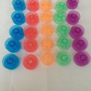 May include: A set of 30 plastic bobbins for sewing machines. The bobbins are in five colors: blue, pink, orange, green, and purple.