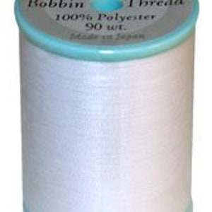 May include: A white spool of The Finishing Touch brand embroidery thread. The spool is labeled "Bobbin Thread 100% Polyester 90 wt. Made in Japan."
