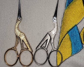 May include: Two pairs of decorative scissors with bird-shaped handles. One pair is gold and the other is silver.