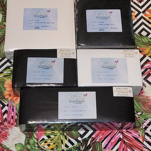 May include: A stack of four black and white boxes with the E-Zee logo and product information. The boxes contain backing and topping for crafts. The boxes are labeled with the Oeko-Tex Standard 100 certification.