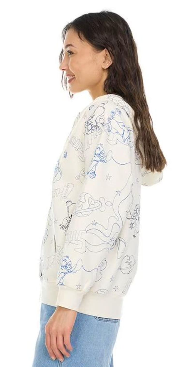 May include: Cream-colored zip-up hoodie with a blue cartoon character outline pattern. The hoodie features a drawstring hood, ribbed cuffs, and a ribbed hem. The design includes stars, planets, and other cartoon elements. The model is wearing blue jeans.