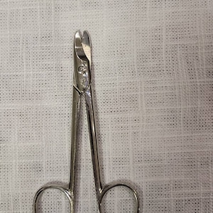 Puede incluir: Tijeras quirúrgicas de plata con hojas curvas y dos anillos.