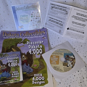 May include: A selection of Dakota Collectibles embroidery design products, including a CD-ROM starter set, brochures, and a CD. The materials feature the brand's logo and the text "Discover Dakota 4,000" with cartoon illustrations.
