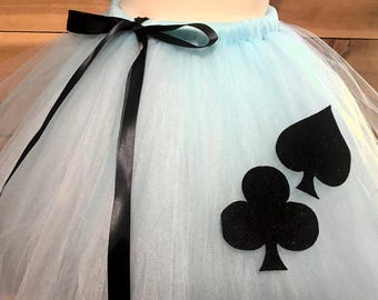 May include: A light blue tulle skirt with a black satin bow and ribbon. The skirt features black spade and club suit symbols. This skirt is suitable for costumes and themed events.