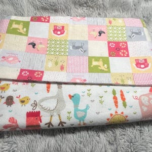 May include: A folded baby blanket with a patchwork design on top and a farm animal print on the bottom. The patchwork features squares with animals and floral patterns in pink, green, and yellow. The bottom has chickens, ducks, and a pig.
