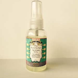 May include: A clear glass bottle with a spray nozzle and a green and white label that reads "The Nutcracker Hair & Body Spray" with the text "Chicomethicone, Bergamot, Orange Natural Fragrance 2oz."