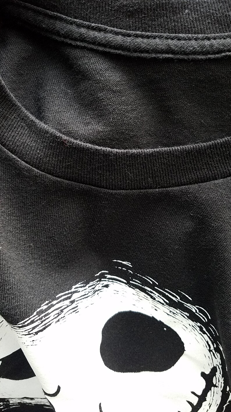 K&ouml;nnte beinhalten: Schwarzes T-Shirt mit einem wei&szlig;en Grafikdruck eines Sch&auml;dels mit einem breiten Grinsen. Der Sch&auml;del ist wei&szlig; umrandet und hat ein schwarzes Auge.