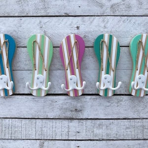 May include: Five wooden flip-flop shaped hooks painted in different colors, including teal, green, pink, and blue. Each hook has a white octopus design with three tentacles on each side.