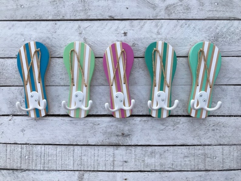 May include: Five wooden flip-flop shaped hooks painted in different colors, including teal, green, pink, and blue. Each hook has a white octopus design with three tentacles on each side.