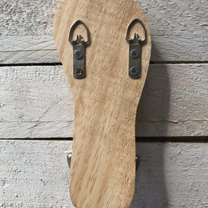 May include: The back of a wooden wall-mounted hanger with two metal hooks and two metal hanging loops.