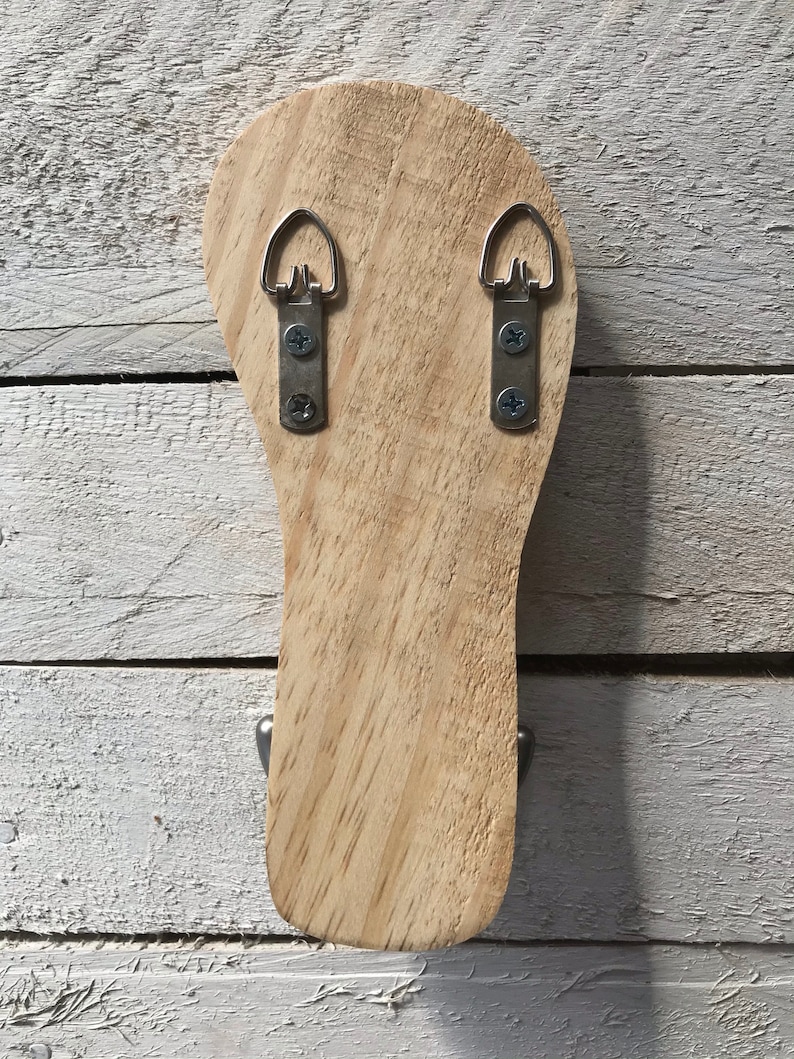 May include: The back of a wooden wall-mounted hanger with two metal hooks and two metal hanging loops.