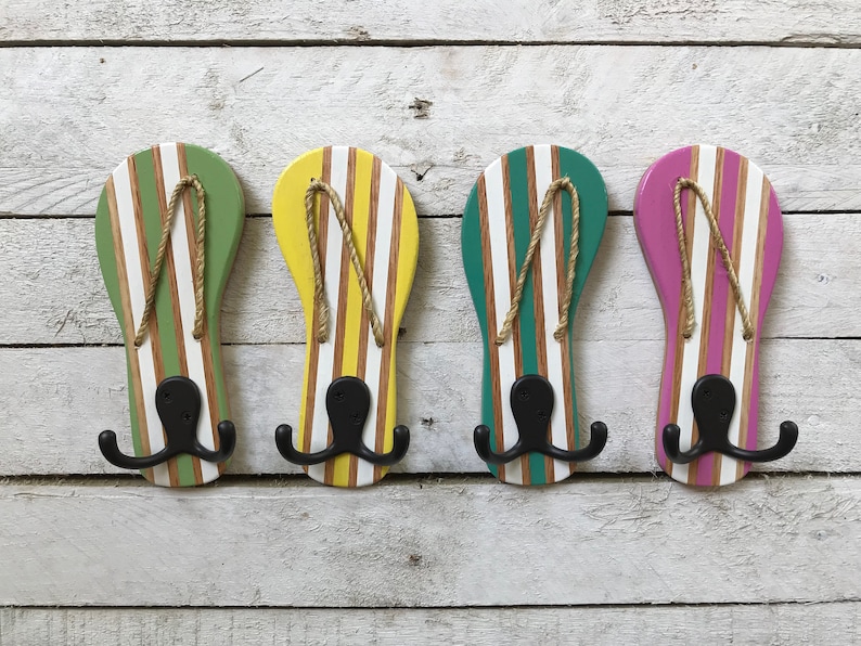May include: Four wooden flip-flop shaped hooks painted in green, yellow, teal, and pink with white stripes. Each hook has a black double hook.