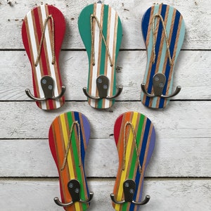 May include: Five wooden flip-flop shaped hooks painted in different colors, including red, green, blue, yellow, and purple. Each hook has a white stripe pattern and a silver metal hook.