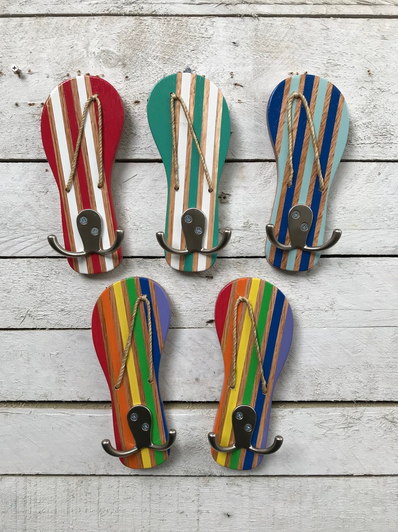 May include: Five wooden flip-flop shaped hooks painted in different colors, including red, green, blue, yellow, and purple. Each hook has a white stripe pattern and a silver metal hook.