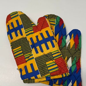 May include: A pair of quilted oven mitts with a vibrant African print. The mitts feature a repeating pattern of yellow, blue, red, and green geometric shapes. The oven mitts are designed for kitchen use.