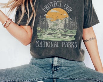 May include: A dark gray t-shirt with a vintage-style graphic of a mountain landscape and the text "Protect Our National Parks".