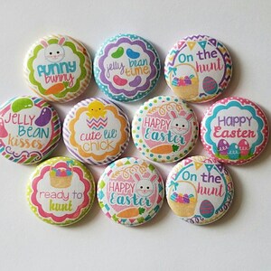 Peut inclure: Un ensemble de dix badges ronds avec des illustrations colorées sur le thème de Pâques. Les motifs incluent des lapins, des poussins, des bonbons et des paniers avec les textes Funny Bunny, Jelly Bean Time, On the hunt, Jelly Bean kisses, cute lil chick et Happy Easter.
