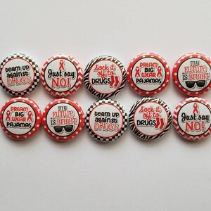 May include: A set of ten circular pin-back buttons featuring red awareness ribbons and various slogans including Team Up Against Drugs, Just Say No, Sock It Off To Drugs, Dream Big Wear Pajamas, and My Future Is Bright with black and white patterns.