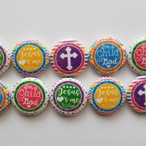 Puede incluir: Diez chapas redondas dispuestas en dos filas. Las chapas presentan bordes de arcoíris coloridos y fondos brillantes. Los diseños incluyen cruces blancas y el texto Jesus loves me o I'm a Child of God con pequeños iconos de corazones.
