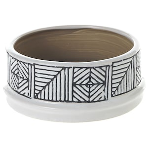 May include: A white ceramic bowl with a black geometric pattern around the exterior. The interior of the bowl is a light brown color. The bowl has a wide, shallow design and a rounded base.