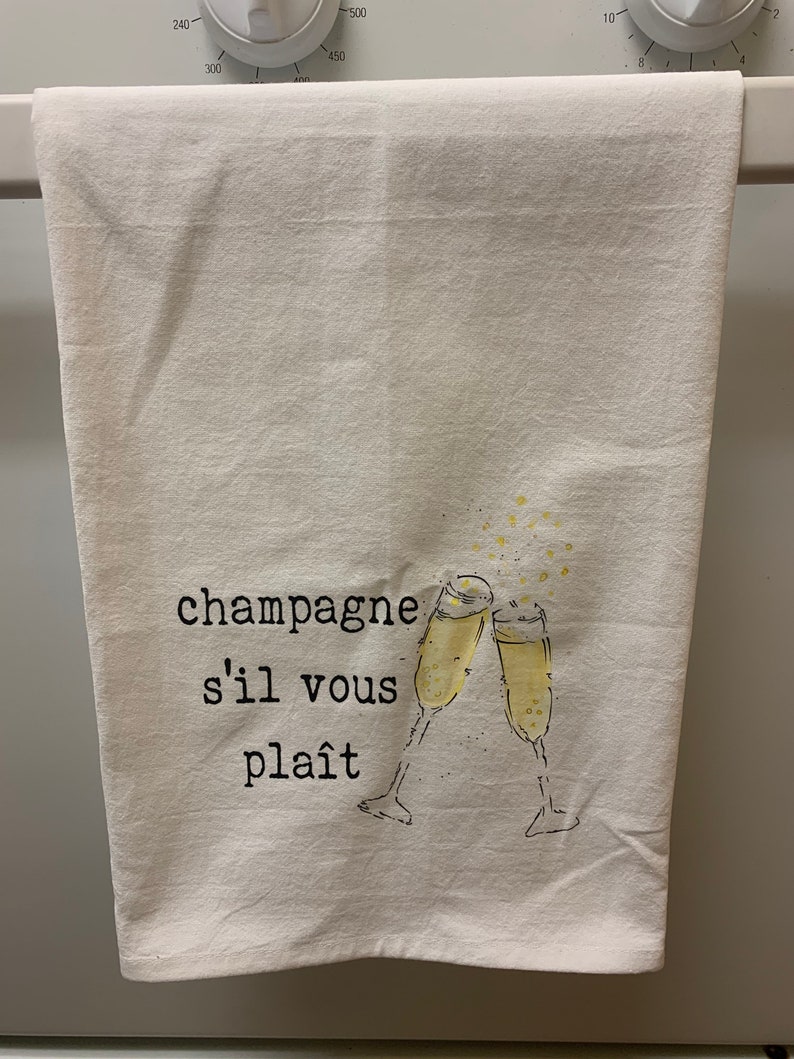 May include: White kitchen towel with the text "champagne s'il vous pla&icirc;t" and a drawing of two champagne glasses clinking.