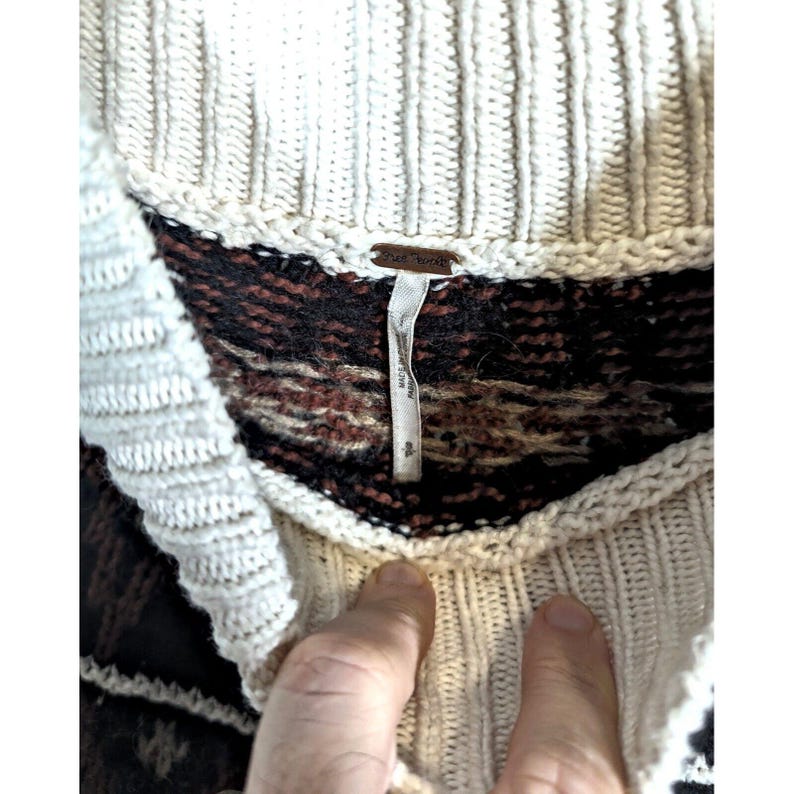 Puede incluir: Su&eacute;ter de punto color crema con un dise&ntilde;o estampado en tonos marrones y negros. El su&eacute;ter tiene un cuello de punto acanalado y una etiqueta que dice "Free People". El su&eacute;ter est&aacute; hecho de un material suave y c&oacute;modo.
