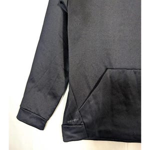 May include: A close-up of a black hoodie with a kangaroo pocket. The sleeve and the bottom hem are visible. The text "DRI-FIT" is printed on the bottom hem.