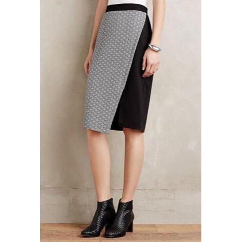 May include: A knee-length pencil skirt with a geometric patterned overlay in gray and white, paired with a solid black panel. The skirt has a high waist and is worn with black ankle boots.