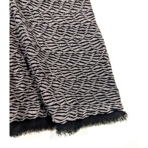 May include: Close-up of a textured fabric with a wave-like pattern in shades of gray and black. The fabric has a fringed edge in black. The material appears to be soft and pliable, suitable for clothing or home decor.