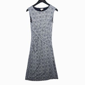Puede incluir: Vestido sin mangas hasta la rodilla con un estampado geom&eacute;trico en blanco y azul marino. El vestido tiene un cuello redondo y est&aacute; colgado de una percha negra. La tela parece ser un material suave y drapeado.
