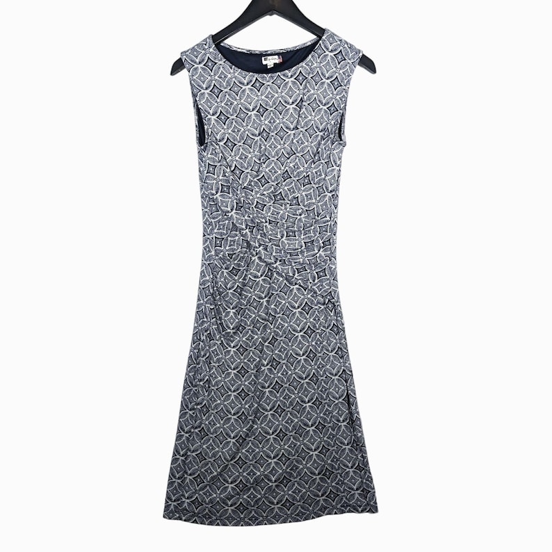 Puede incluir: Vestido sin mangas hasta la rodilla con un estampado geom&eacute;trico en blanco y azul marino. El vestido tiene un cuello redondo y est&aacute; colgado de una percha negra. La tela parece ser un material suave y drapeado.